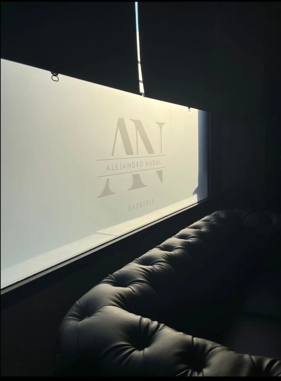 Zona de espera con sofá y el rótulo Alejandro Nadal Barbería en el cristal